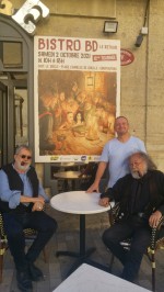 François Corteggiani devant l'affiche du "Bistro BD" 2021, en compagnie du patron du bar et de son ami, complice et collègue Pierre Dubois.