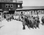 Enfants escortés par des soldats américains, sortant par la porte principale du camp, pour se rendre à un hôpital américain (17 avril 1945).